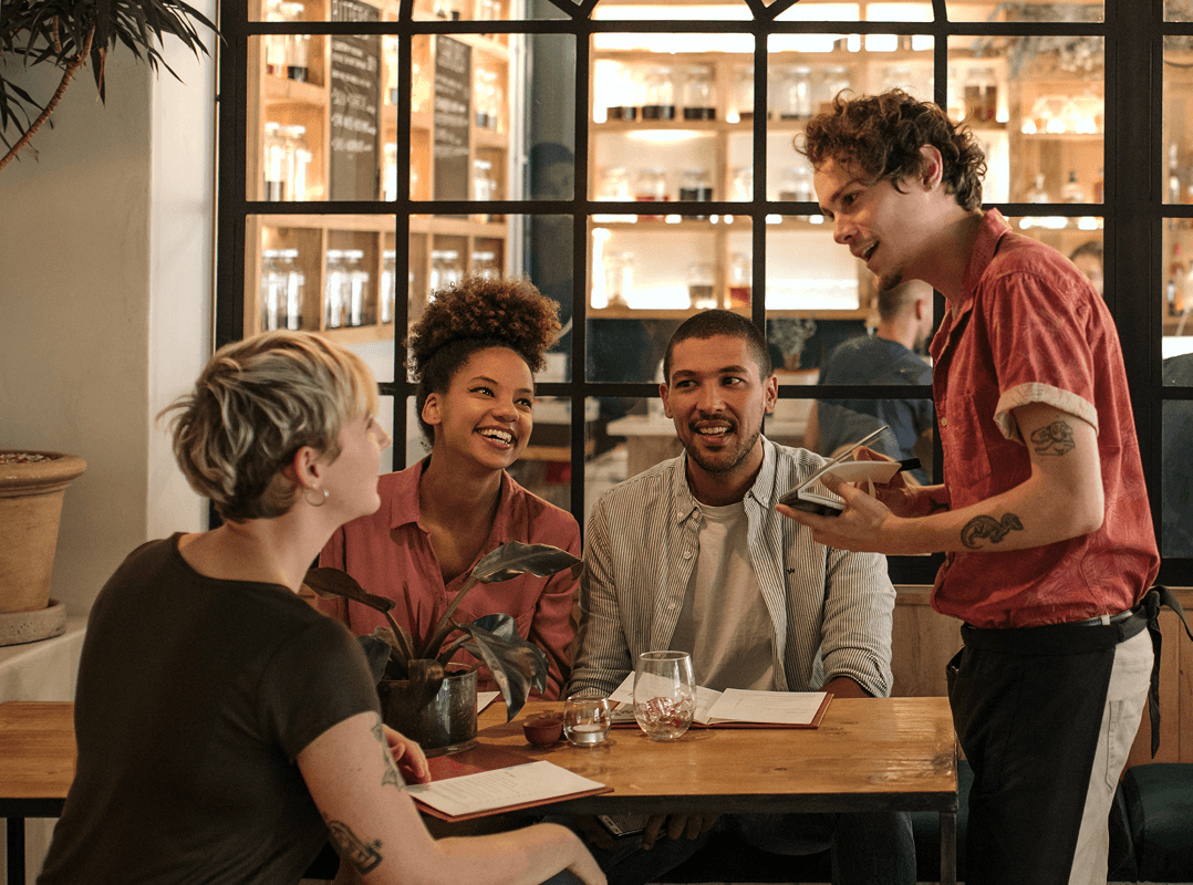 Group of friends practise a new language they have learned as they order from a waiter in a stylish cafe.